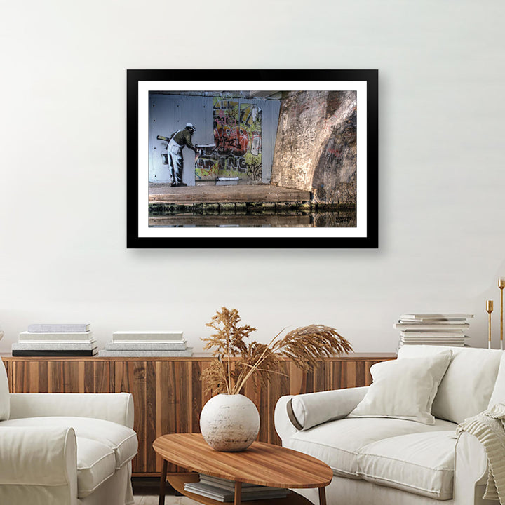 WallPaper man, a framed print of Banksy's Graffiti-Homekor Mounted in a cozy room